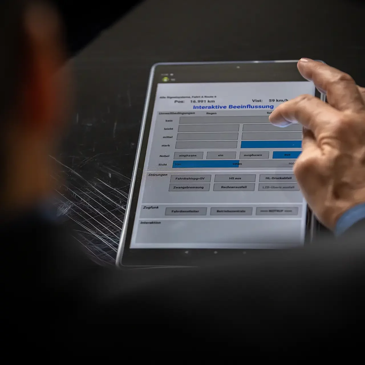 Ausbilderbildschirm des Simulators auf einem Tablet, mit einer Hand bei der Bedienung